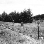 Grenzverlauf durch Schilder, neue Grenzsteine und eine Holzbarriere vor der auf DDR-Gebiet stehenden Grenzsäule gekennzeichnet.